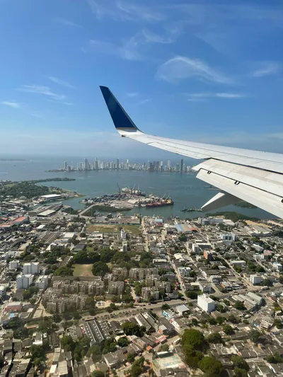 Aerial view of a sprawling city with an airplane wing in the frame, over the sea.