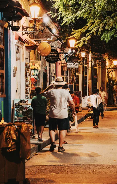 Bustling street in Cartagena at night with people and colorful shops.