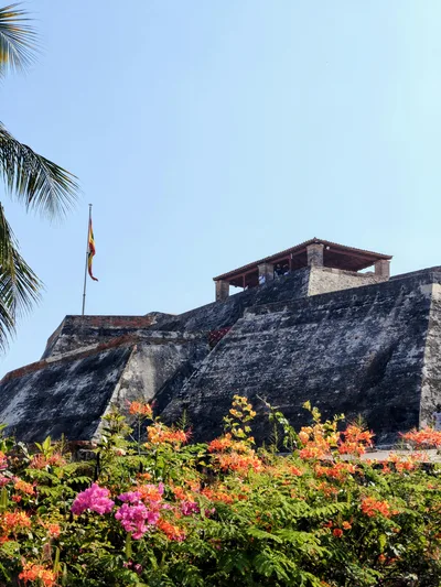 The historic Castillo de San Felipe in Cartagena, Colombia is captured with vibrant flowers in the foreground.