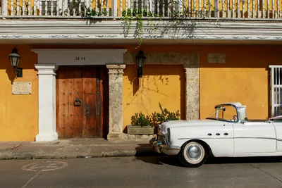 Classic white convertible parked in front of a historic, colorful building facade under daylight.
