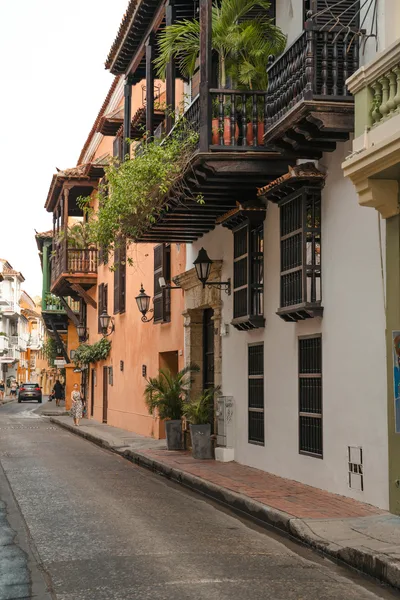A picturesque colonial street featuring colorful buildings, wooden balconies, and lush plants.