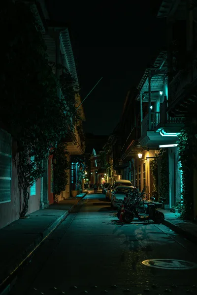 Nighttime view of a quaint street in Cartagena, Colombia with parked vehicles and illuminated colonial architecture.