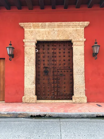 Rustic colonial-style doorway on a vibrant red wall in Cartagena, Colombia.