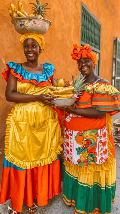 Two women in vibrant traditional attire holding fruit in Cartagena, Colombia.